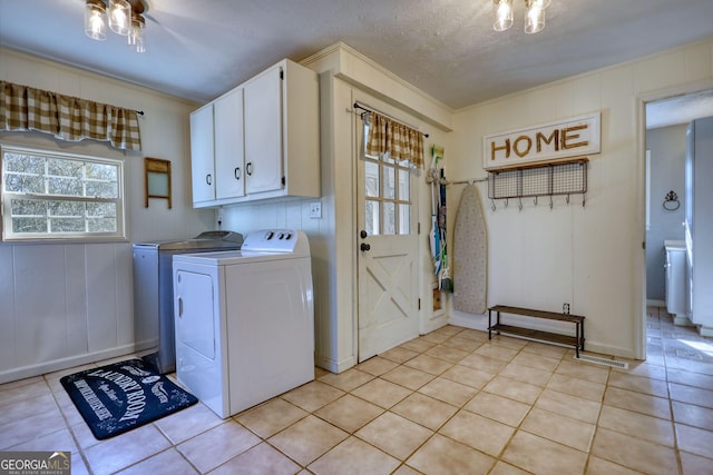 laundry room featuring light tile patterned flooring, cabinets, a textured ceiling, ornamental molding, and washer and clothes dryer