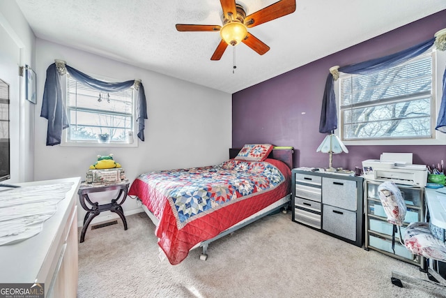 bedroom with ceiling fan, light colored carpet, and a textured ceiling