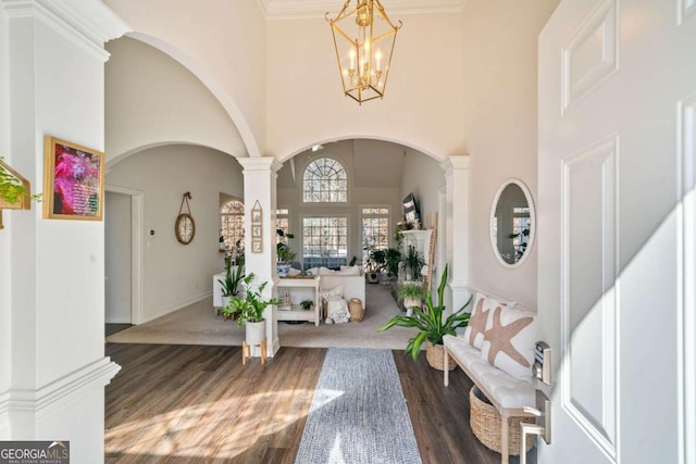 entrance foyer featuring a high ceiling, dark wood-type flooring, a chandelier, and ornate columns