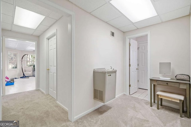 hallway with a paneled ceiling and light carpet