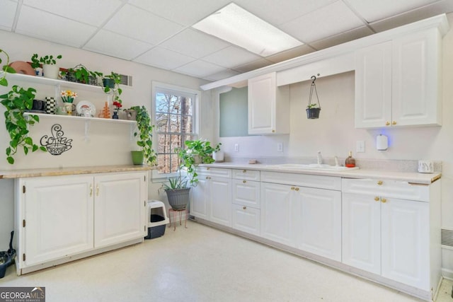 kitchen with sink, a paneled ceiling, and white cabinets