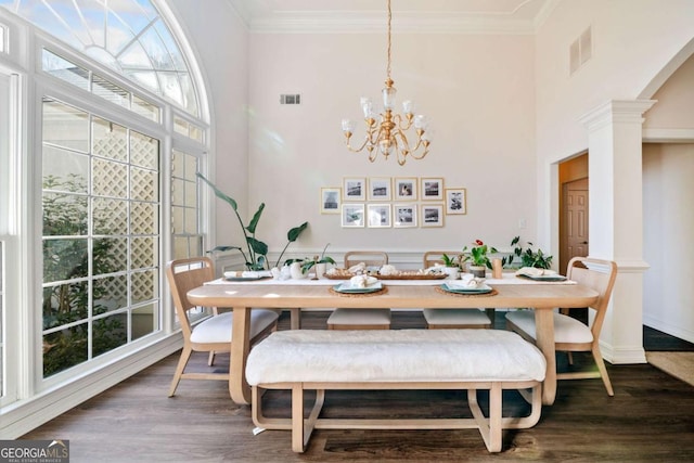 dining room featuring decorative columns, ornamental molding, dark hardwood / wood-style floors, and a high ceiling