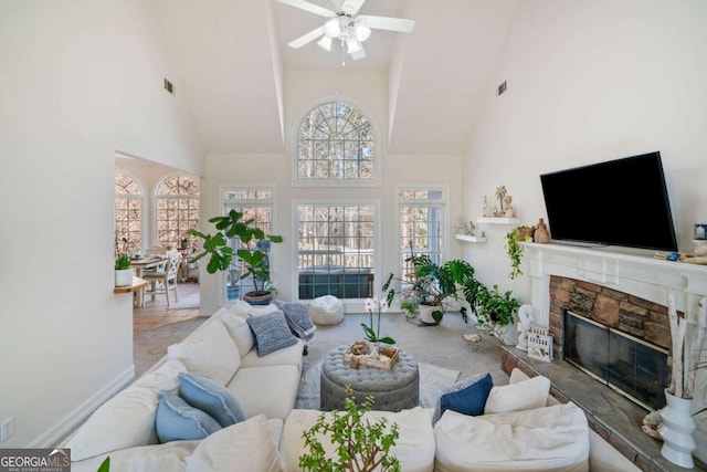 living room with ceiling fan, a stone fireplace, high vaulted ceiling, and light carpet