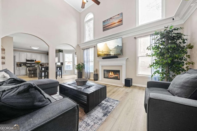 living room featuring crown molding, ceiling fan, high vaulted ceiling, and light hardwood / wood-style flooring