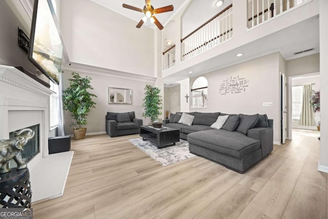 living room featuring crown molding, a towering ceiling, ceiling fan, and light hardwood / wood-style flooring