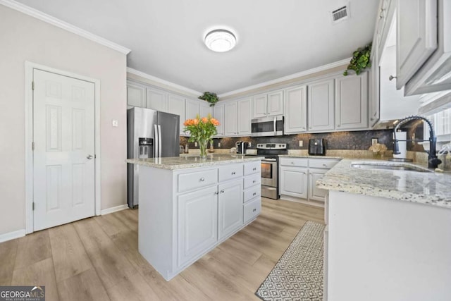 kitchen with sink, stainless steel appliances, ornamental molding, an island with sink, and light stone countertops