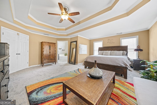 bedroom featuring ensuite bathroom, ornamental molding, ceiling fan, a tray ceiling, and light carpet