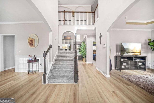 foyer with crown molding, a towering ceiling, and light wood-type flooring