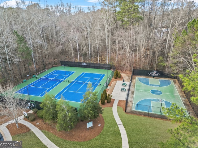 view of tennis court with basketball hoop and a lawn