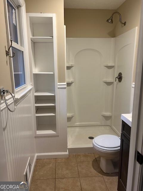 bathroom with vanity, tile patterned floors, toilet, and a shower