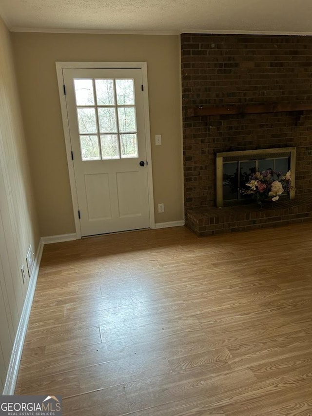 doorway featuring a brick fireplace, ornamental molding, light hardwood / wood-style floors, and a textured ceiling