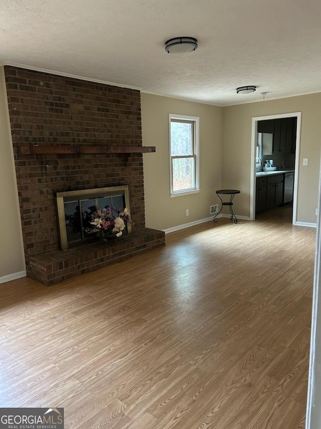 unfurnished living room featuring hardwood / wood-style floors, a textured ceiling, and a brick fireplace