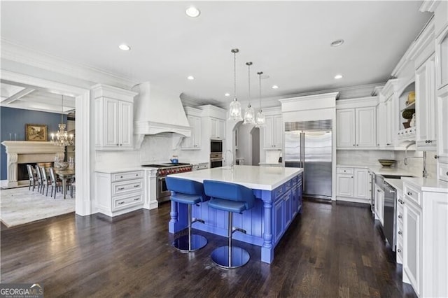 kitchen featuring a breakfast bar area, white cabinetry, built in appliances, custom range hood, and a kitchen island