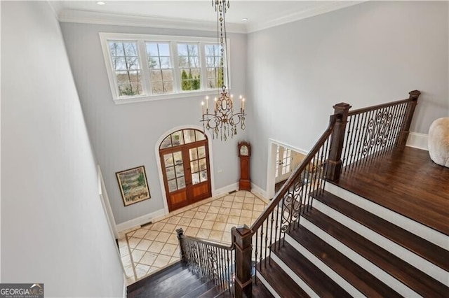 entryway with french doors, ornamental molding, a high ceiling, and a notable chandelier