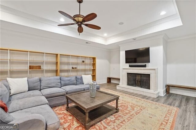 living room with ceiling fan, ornamental molding, a tray ceiling, and wood-type flooring