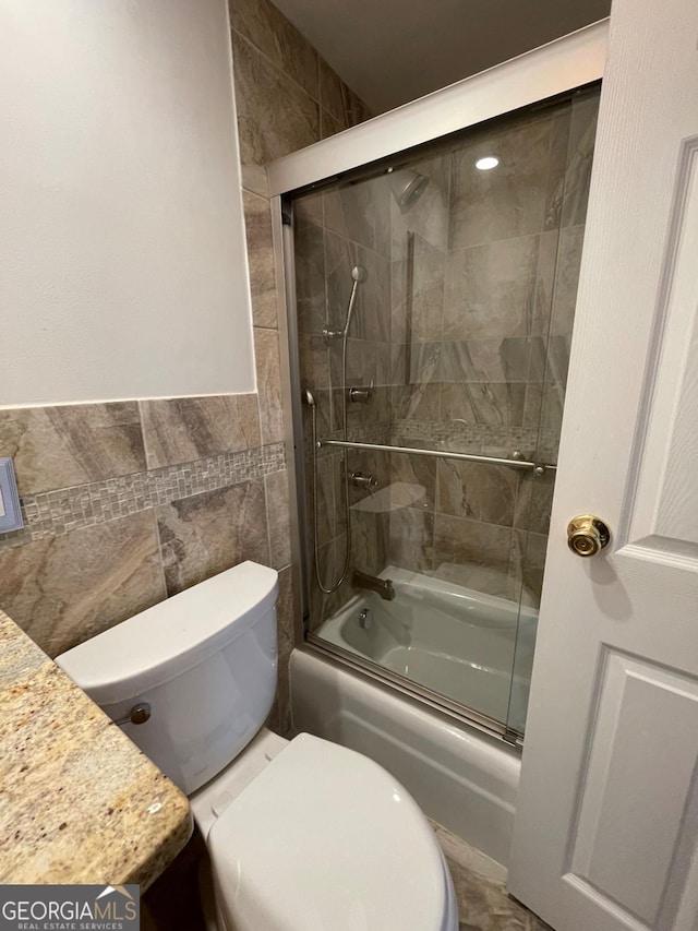 bathroom featuring tile walls, enclosed tub / shower combo, and toilet