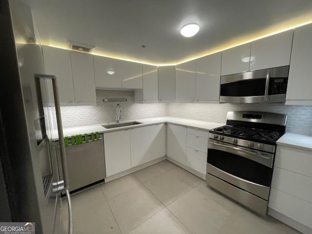 kitchen featuring sink, light tile patterned floors, white cabinetry, backsplash, and stainless steel appliances