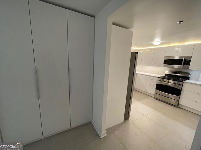 kitchen with stainless steel appliances, light tile patterned floors, white cabinets, and backsplash