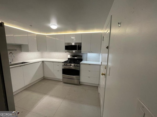 kitchen featuring light tile patterned flooring, sink, appliances with stainless steel finishes, white cabinets, and backsplash