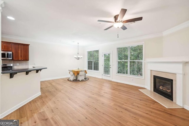 living room featuring ornamental molding, a high end fireplace, ceiling fan with notable chandelier, and light wood-type flooring