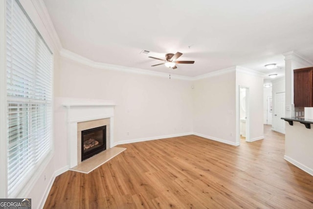 unfurnished living room featuring crown molding, light wood-type flooring, a wealth of natural light, ceiling fan, and a fireplace