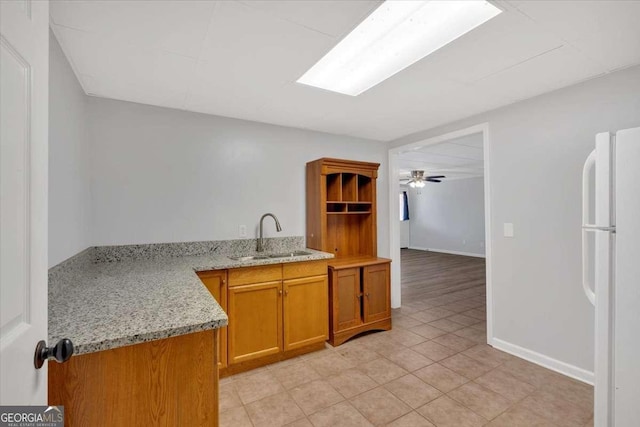 kitchen with sink, white fridge, light tile patterned floors, light stone counters, and kitchen peninsula