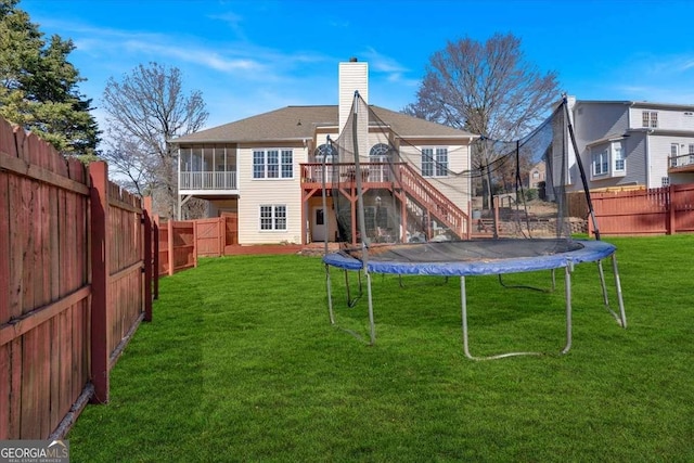 rear view of house with a deck, a trampoline, and a lawn