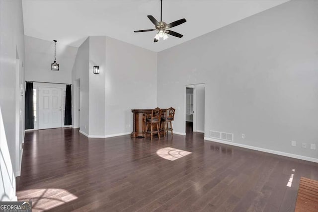 unfurnished living room featuring dark hardwood / wood-style flooring, a towering ceiling, ceiling fan, and bar