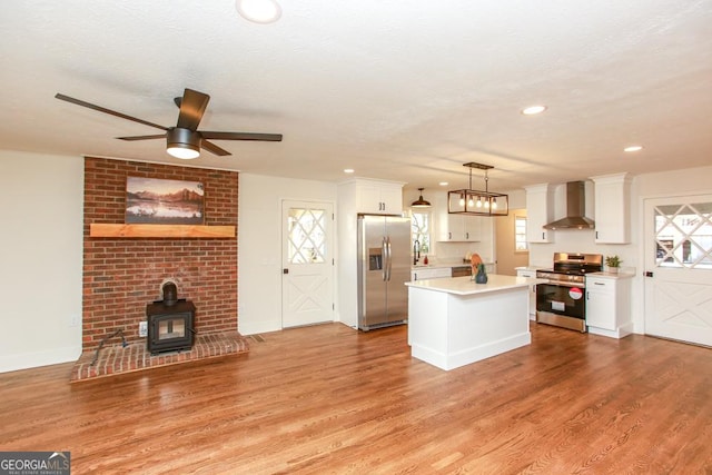 kitchen with wall chimney exhaust hood, white cabinetry, a wood stove, pendant lighting, and stainless steel appliances