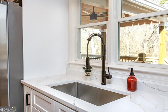 room details with white cabinetry, light stone countertops, sink, and stainless steel fridge