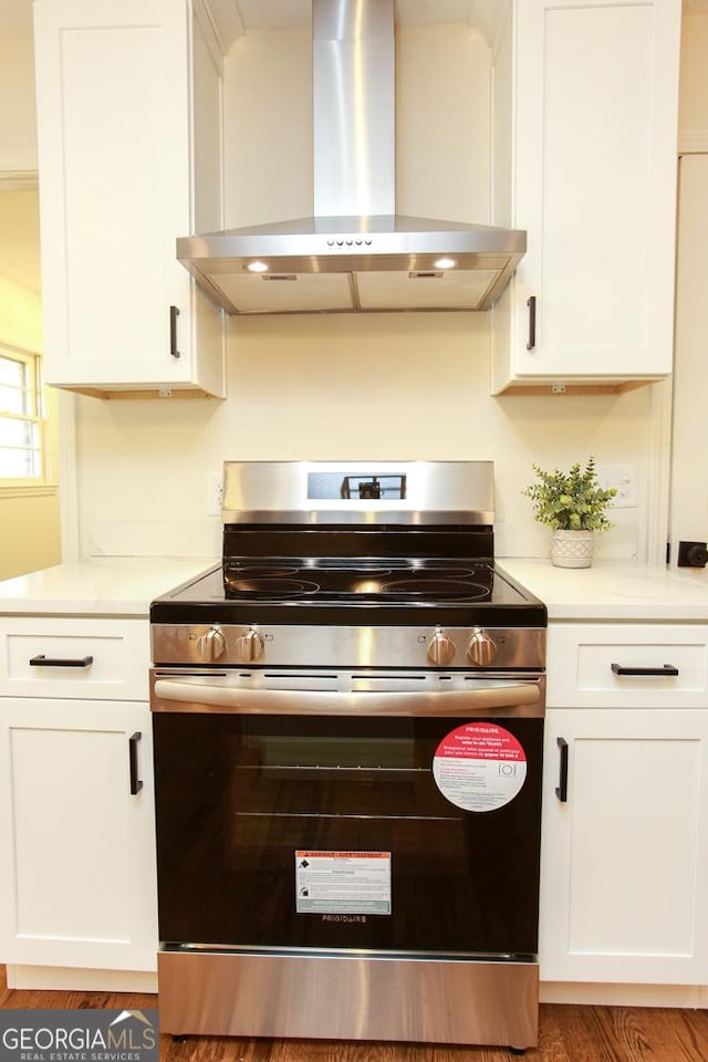 kitchen with electric stove, wall chimney range hood, and white cabinetry