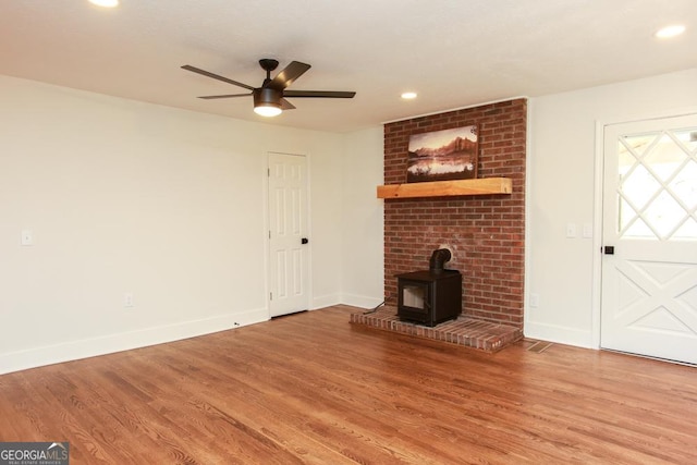 unfurnished living room featuring wood-type flooring, ceiling fan, and a wood stove