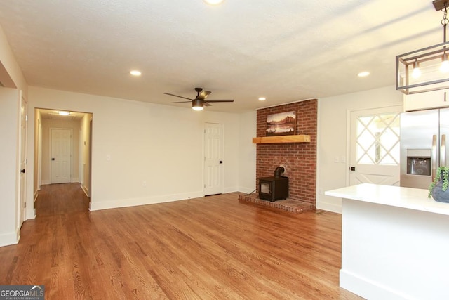 unfurnished living room featuring ceiling fan, wood-type flooring, and a wood stove