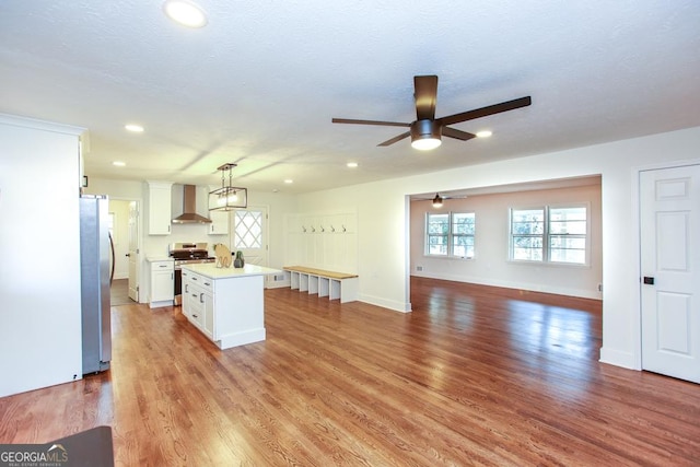 kitchen featuring a kitchen island, pendant lighting, white cabinets, stainless steel appliances, and wall chimney exhaust hood