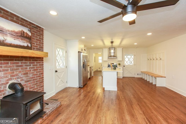 kitchen featuring light wood-type flooring, a wood stove, pendant lighting, stainless steel appliances, and white cabinets