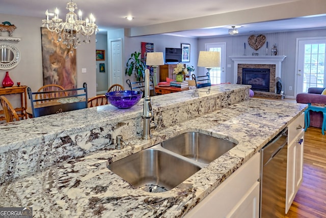 kitchen with sink, decorative light fixtures, light hardwood / wood-style flooring, stainless steel dishwasher, and light stone countertops