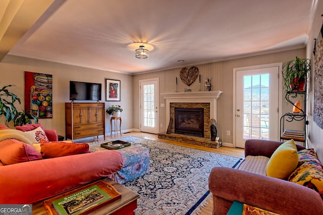 living room with crown molding, a stone fireplace, and light wood-type flooring