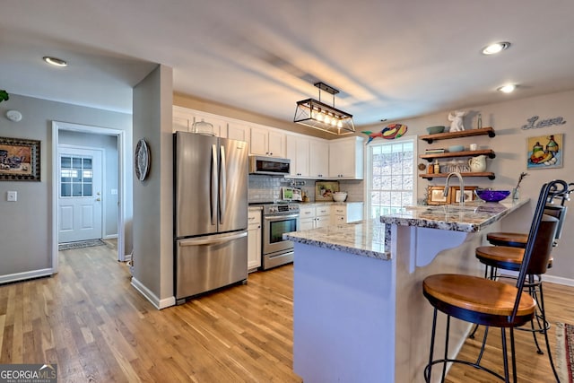 kitchen with white cabinets, a kitchen breakfast bar, kitchen peninsula, stainless steel appliances, and light stone countertops