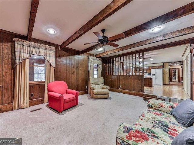 carpeted living room featuring ceiling fan, wooden walls, and beam ceiling