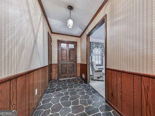 doorway to outside featuring crown molding, wooden walls, and a textured ceiling