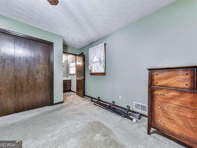 unfurnished bedroom with light colored carpet, a textured ceiling, and ensuite bathroom