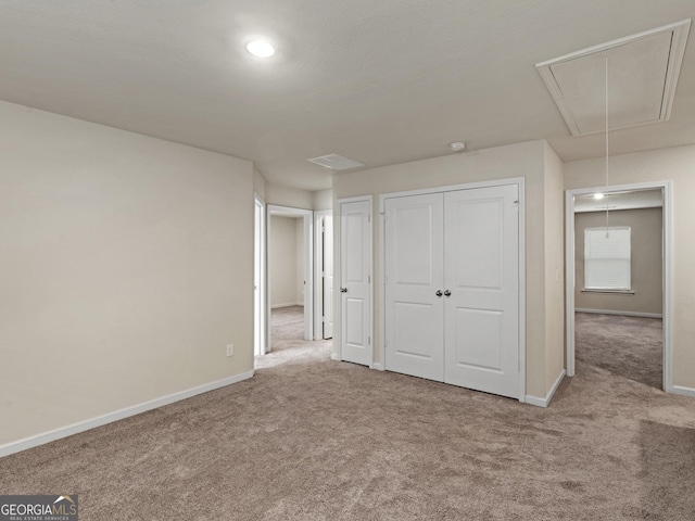 unfurnished bedroom featuring carpet floors, attic access, baseboards, and a closet