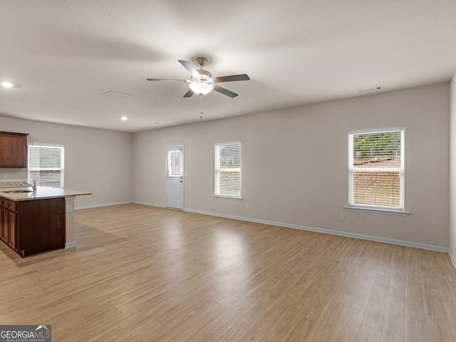 unfurnished living room featuring light wood finished floors, visible vents, baseboards, ceiling fan, and a sink