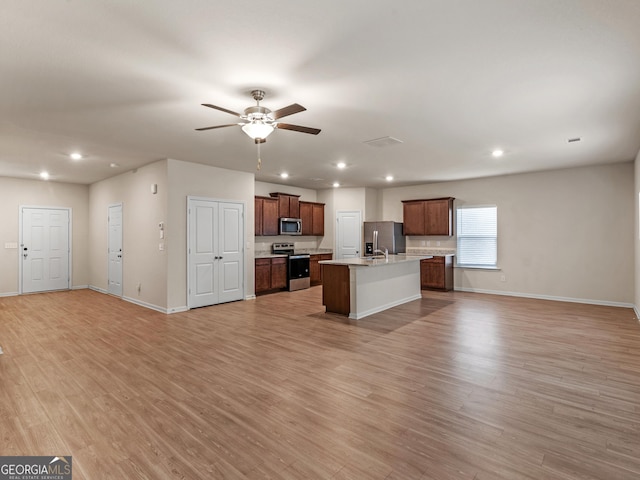 kitchen with an island with sink, ceiling fan, open floor plan, stainless steel appliances, and light wood-type flooring