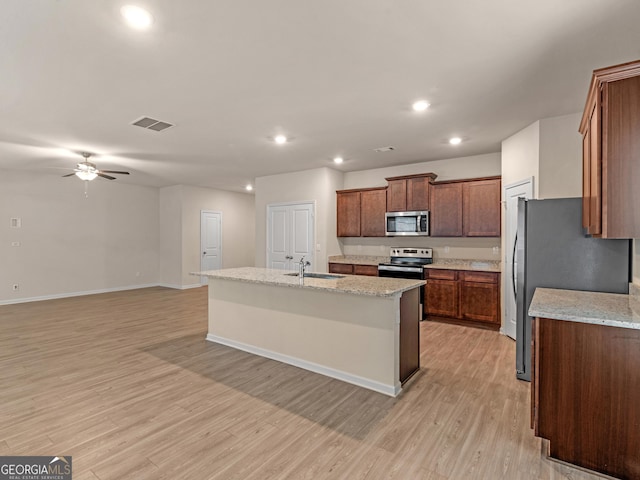 kitchen with a kitchen island with sink, stainless steel appliances, a sink, visible vents, and light wood-style floors