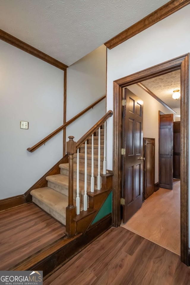 staircase with ornamental molding, wood-type flooring, and a textured ceiling