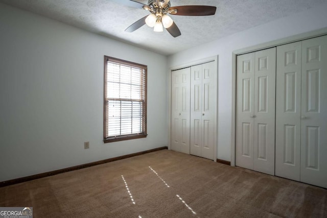 unfurnished bedroom featuring ceiling fan, light colored carpet, a textured ceiling, and two closets