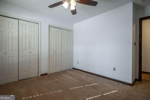 unfurnished bedroom with light carpet, ceiling fan, two closets, and a textured ceiling