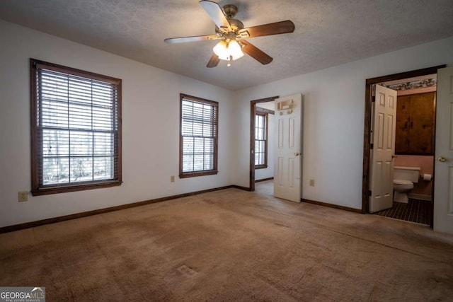 unfurnished bedroom featuring ceiling fan, ensuite bathroom, a textured ceiling, and carpet