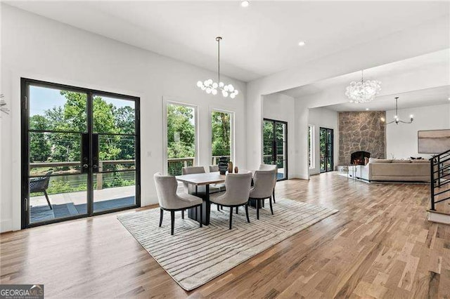 dining room with an inviting chandelier, a stone fireplace, and light hardwood / wood-style flooring